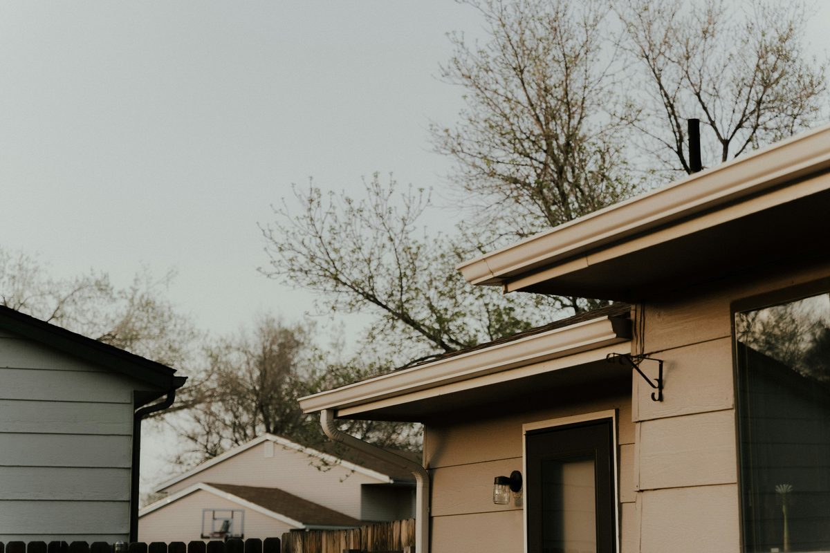 Suburban Midwestern house with aluminum gutters and downspout, mature trees behind the roofline